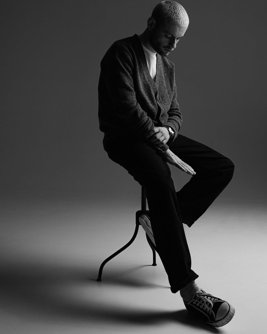 A man seated on a stool, head bowed, in quiet shadow